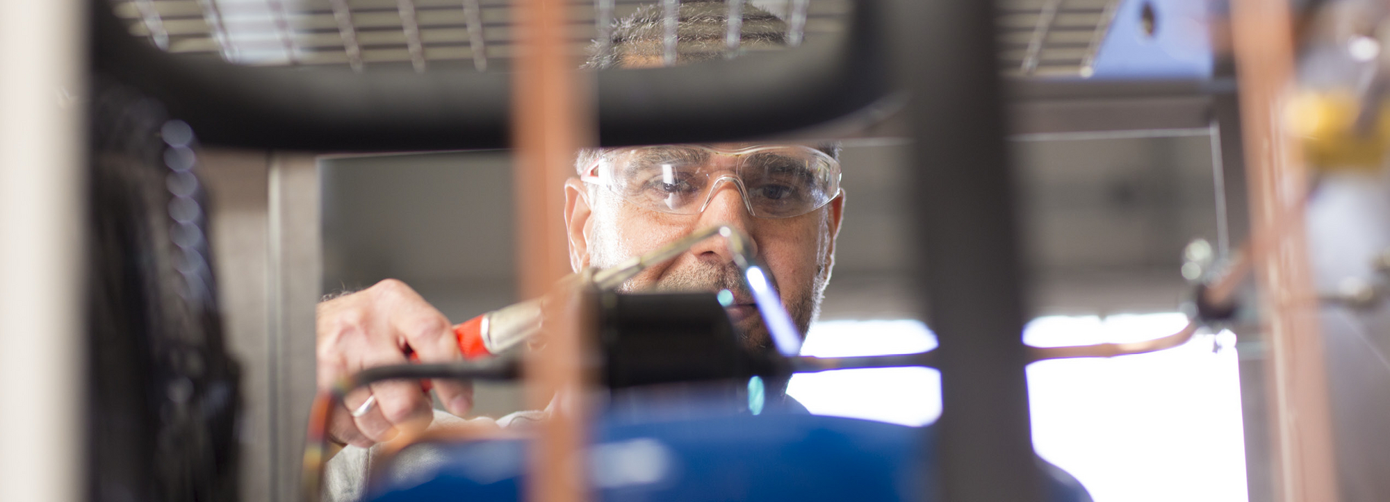 Ein Mann mit Schweißbrenner schweißt Leitungen eines Kühlaggregates zusammen.