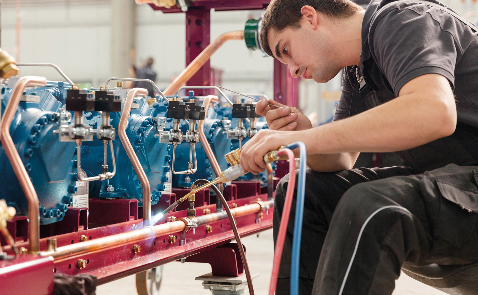 Ein Mitarbeiter schweißt an einem blauen Kühlaggregat in der Produktionshalle.